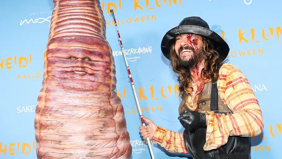 Heidi Klum Halloween 2022 Heidi Klum steht im riesigen Wurmkostüm neben einem Mann mit Angel, schwarzem Hut, Wathose und blutiger Gesichtsschminke.