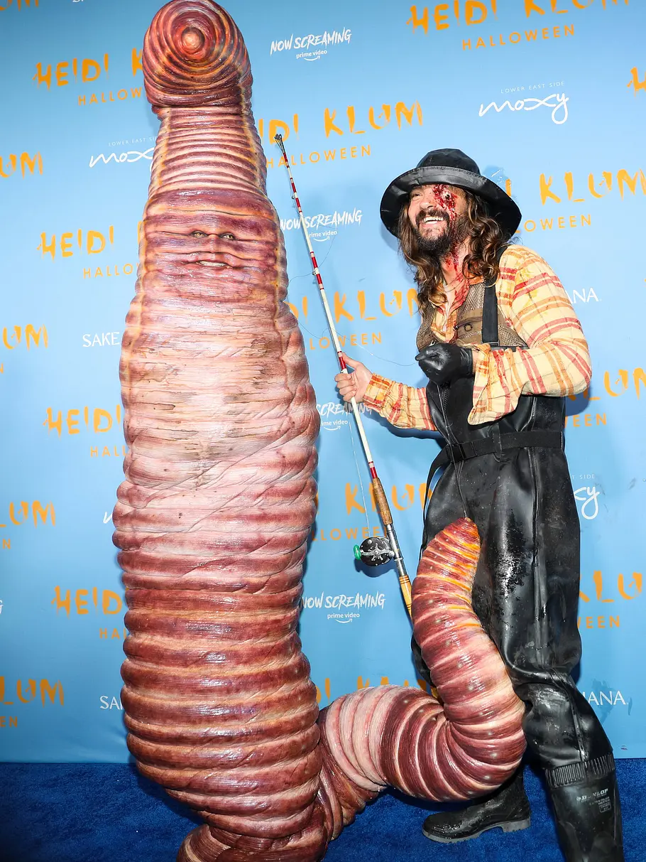 Heidi Klum zu Halloween 2022 als Wurm Heidi Klum an Halloween 2022 im riesigen Wurmkostüm steht neben Tom Kaulitz, der als Angler mit Angelrute und blutig geschminktem Gesicht posiert.
