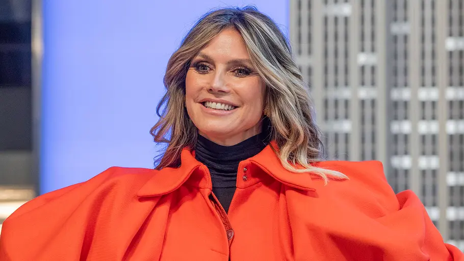 Heidi Klum Halloween Kostüm Heidi Klum lächelt in einer leuchtend roten Jacke mit voluminösen Schultern über einem schwarzen Rollkragenoberteil.