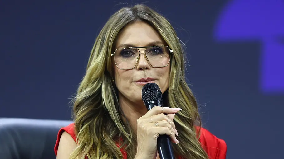 Heidi Klum Heidi Klum trägt eine Brille und ein rotes Kleid und spricht in ein Mikrophon.