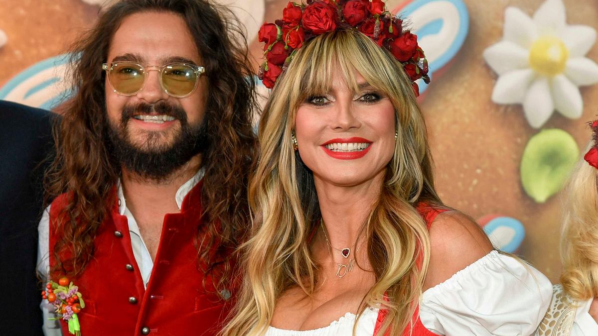 Heidi Klum mit Ehemann Tom Kaulitz: Beide tragen festliche Wiesn-Tracht in Weiß und Rot und lächeln in die Kamera. Heidi schmückt ein roter Blumenkranz, passend zu ihrem Kleid.