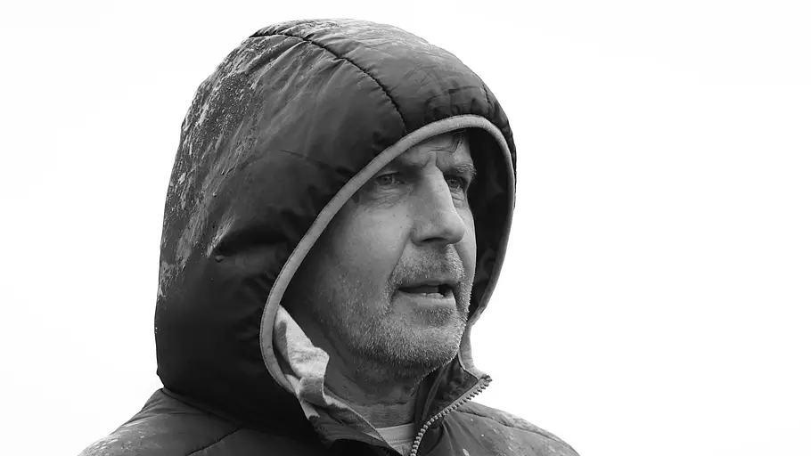 Heiko Weber Todesursache Ein Schwarz-Weiß-Foto zeigt Heiko Weber 2023 mit Kapuze im Regen am Rande eines Fußballspiels.