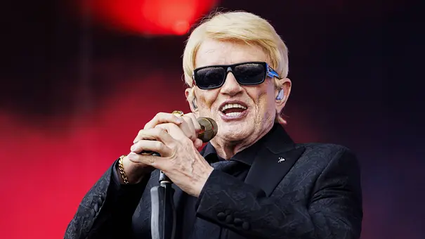 Heino singt mit Sonnenbrille und schwarzem Anzug in ein Mikrofon vor rot beleuchtetem Hintergrund. - Foto: IMAGO / NL Beeld Heino singt mit Sonnenbrille und schwarzem Anzug in ein Mikrofon vor rot beleuchtetem Hintergrund. - Foto: IMAGO / NL Beeld