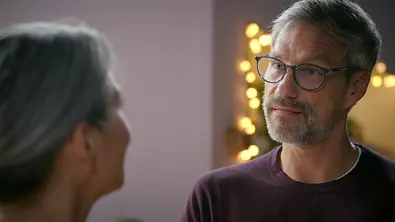 Henning trägt eine Brille und schaut Daniela an, die unscharf im Vordergrund steht. Im Hintergrund leuchten warme Lichter. - Foto: RTL Henning trägt eine Brille und schaut Daniela an, die unscharf im Vordergrund steht. Im Hintergrund leuchten warme Lichter. - Foto: RTL