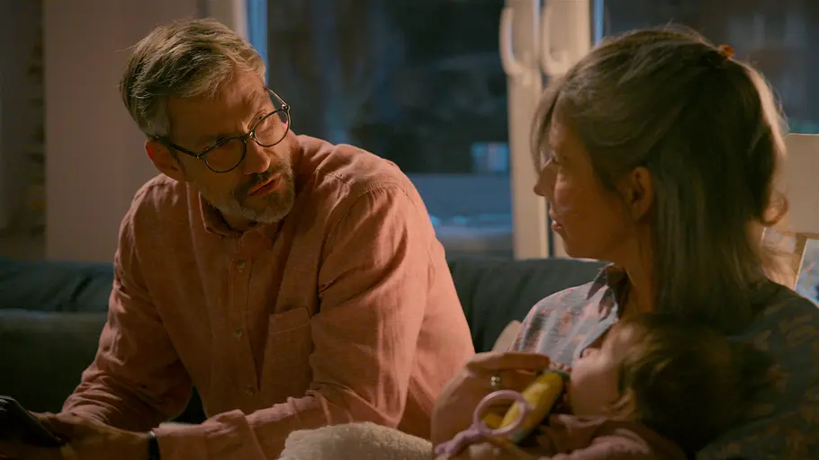 Henning Daniela AWZ Henning trägt eine Brille und ein rosafarbenes Hemd. Neben ihm hält Daniela ein Kind mit einem Beißring im Arm.