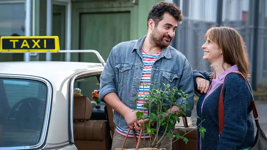 „Heute fängt mein neues Leben an“: Baris und Amelie Baris und Amelie neben einem Taxi, während der Mann eine Pflanze in den Händen hält.