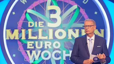 Günther Jauch steht mit Brille, Anzug und Moderationskarte vor dem bunten Schriftzug „Die 3 Millionen Euro Woche“. - Foto: RTL / Stefan Gregorowius Günther Jauch steht mit Brille, Anzug und Moderationskarte vor dem bunten Schriftzug „Die 3 Millionen Euro Woche“. - Foto: RTL / Stefan Gregorowius