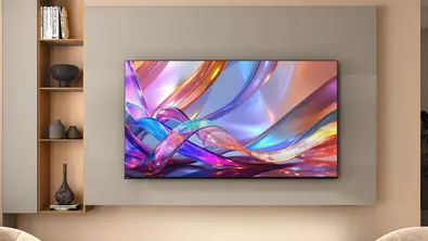 Ein flach an der Wand montierter Fernseher zeigt ein farbenfrohes, abstraktes Bild mit geschwungenen Linien in Blau, Pink und Orange. Daneben befindet sich ein offenes Regal mit dekorativen Vasen und Büchern. - Foto: Amazon/PR Ein flach an der Wand montierter Fernseher zeigt ein farbenfrohes, abstraktes Bild mit geschwungenen Linien in Blau, Pink und Orange. Daneben befindet sich ein offenes Regal mit dekorativen Vasen und Büchern. - Foto: Amazon/PR