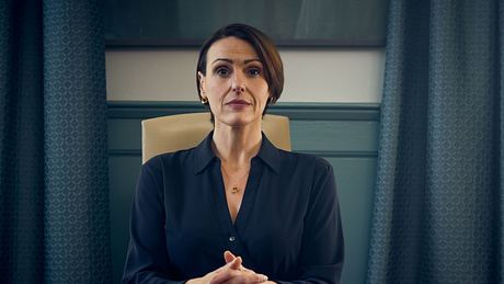 Die Schauspielerin Suranne Jones sitzt an einem Schreibtisch und schaut in die Kamera. - Foto: Des Willie/Netflix © 2025