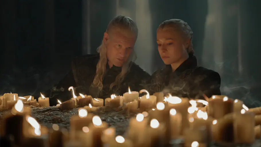 Rhaenyra und Daemon hocken vor Kerzen. Während ihr Blick nach unten gerichtet ist, lehnt Daemon sich zu seiner Frau.