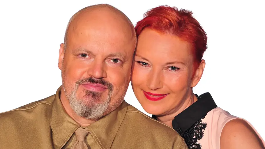 Hubert Kah und Ilona Magyar Hubert Kah in goldfarbenem Hemd mit Krawatte und Ilona Magyar mit kurzen roten Haaren posieren eng nebeneinander.