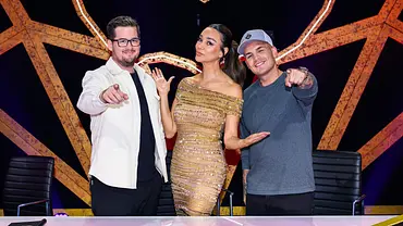 Chris Tall, Verona Pooth und Pietro Lombardi posieren hinter einem Pult vor einer orangefarbenen, leuchtenden Maskenkulisse. - Foto: Joyn Chris Tall, Verona Pooth und Pietro Lombardi posieren hinter einem Pult vor einer orangefarbenen, leuchtenden Maskenkulisse. - Foto: Joyn