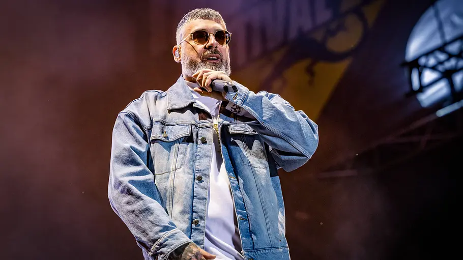 Paul Würdig alias Sido steht mit Sonnenbrille und Jeansjacke auf einer Bühne und hält ein Mikrofon nahe an den Mund.