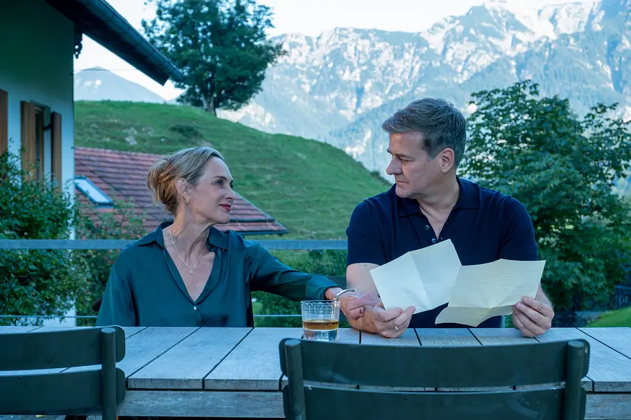 Einfach Elli Einfach Elli - Verzeihen: Vor einer Berglandschaft: Die Eheleute Dr. Diana Sorell (Sophie von Kessel) und Dr. Mark Sorell (Marcus Mittermeier) sitzen auf ihrer Terrasse. Mark Sorell hält zwei Papiere in seinen Händen und richtet den Blick zu seiner Frau.