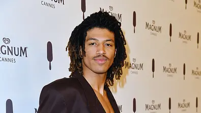 Henry Samuel posiert bei einem Event von Magnum in Cannes vor einer hellen Werbewand mit wiederholtem Magnum-Logo. Er trägt einen dunklen, offenen Blazer und blickt selbstbewusst in die Kamera; seine lockigen Haare und der auffällige Schnurrbart fallen sofort ins Auge. - Foto: IMAGO Henry Samuel posiert bei einem Event von Magnum in Cannes vor einer hellen Werbewand mit wiederholtem Magnum-Logo. Er trägt einen dunklen, offenen Blazer und blickt selbstbewusst in die Kamera; seine lockigen Haare und der auffällige Schnurrbart fallen sofort ins Auge. - Foto: IMAGO