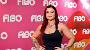Sophia Thiel posiert mit den Händen an den Hüften im schwarzen Top vor einer pinken FIBO-Wand. Ihre Arme sind tätowiert. - Foto: Imago/Panama Pictures Sophia Thiel posiert mit den Händen an den Hüften im schwarzen Top vor einer pinken FIBO-Wand. Ihre Arme sind tätowiert. - Foto: Imago/Panama Pictures