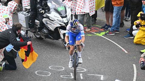 Florian Lipowitz fährt den Berg bei der 18. Etappe der Tour de France hoch und wird von Fans mit Deutschland-Fahne umzingelt. - Foto: IMAGO / Sirotti