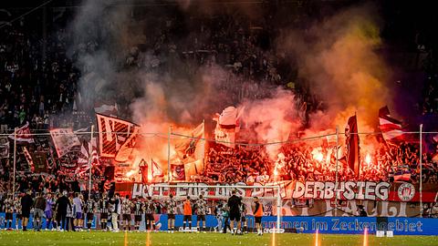 St. Pauli fans fordern per Spruchband Derbysieg mit Pyrofackeln im Hintergrund - Foto:  IMAGO / Philipp Szyza