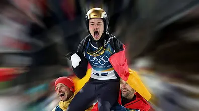 RAIMUND Philipp der am 09.02.2026 auf der Normalschanze Olympiasieger im Skispringen wurde, hier auf den Schultern seiner Teamkollegen, Hoffmann und Paschke beim Jubelschrei mit der Deutschland Fahne, der Hintergrund wurde dynamisch angepasst - Foto: IMAGO / Ulrich Wagner