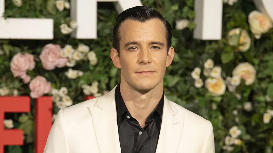 Luke Thompson steht vor einer Fotowand der Netflix-Serie „Bridgerton“.
