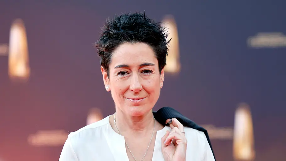 Dunja Hayali lächelt in die Kamera. Sie trägt eine weiße Bluse und hängt sich mit dem Finger ein schwarzes Jacket über die Schulter. Dunja Hayali