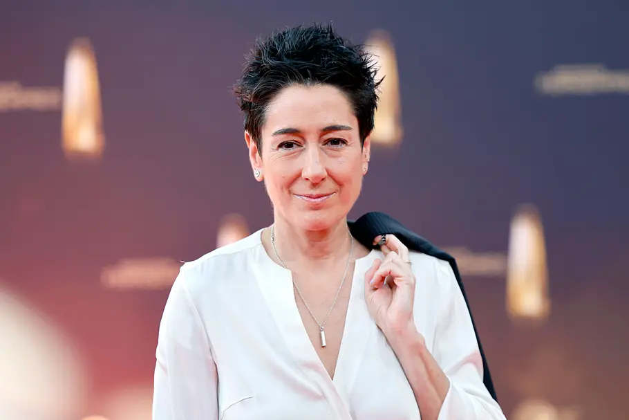 Dunja Hayali Dunja Hayali lächelt in die Kamera. Sie trägt eine weiße Bluse und hängt sich mit dem Finger ein schwarzes Jacket über die Schulter.