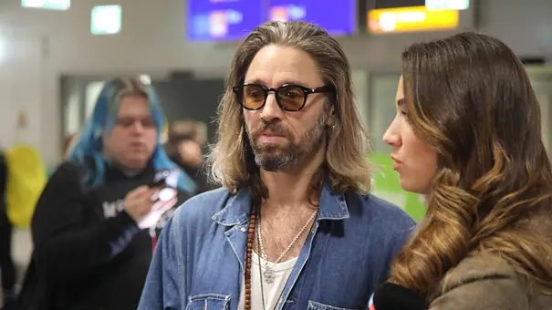 Gil Ofarim steht mit Sonnenbrille am Frankfurter Flughafen. Neben ihm sind zwei weitere Personen zu sehen. - Foto: IMAGO / Matthias Wehnert Gil Ofarim steht mit Sonnenbrille am Frankfurter Flughafen. Neben ihm sind zwei weitere Personen zu sehen. - Foto: IMAGO / Matthias Wehnert
