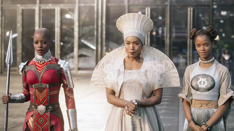 Black Panther Okoye, Königin Ramonda und Shuri stehen vor einem Gebäude mit Glastüren.