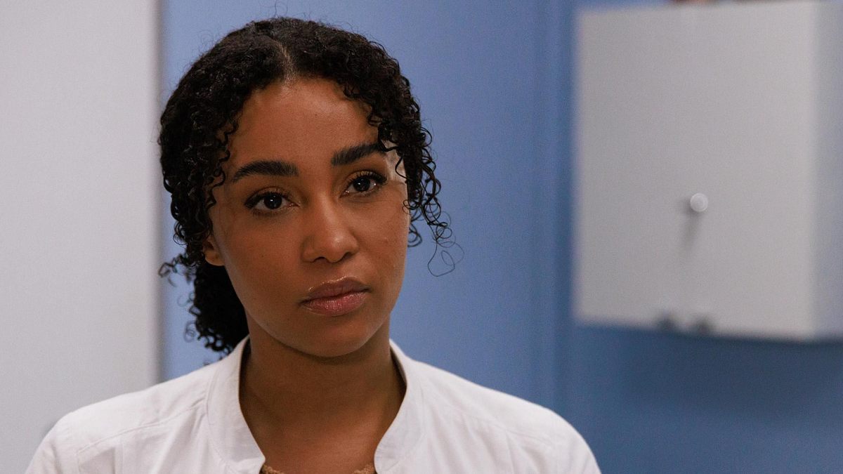 Imani im Krankenhaus-Outfit und mit ernstem Blick.