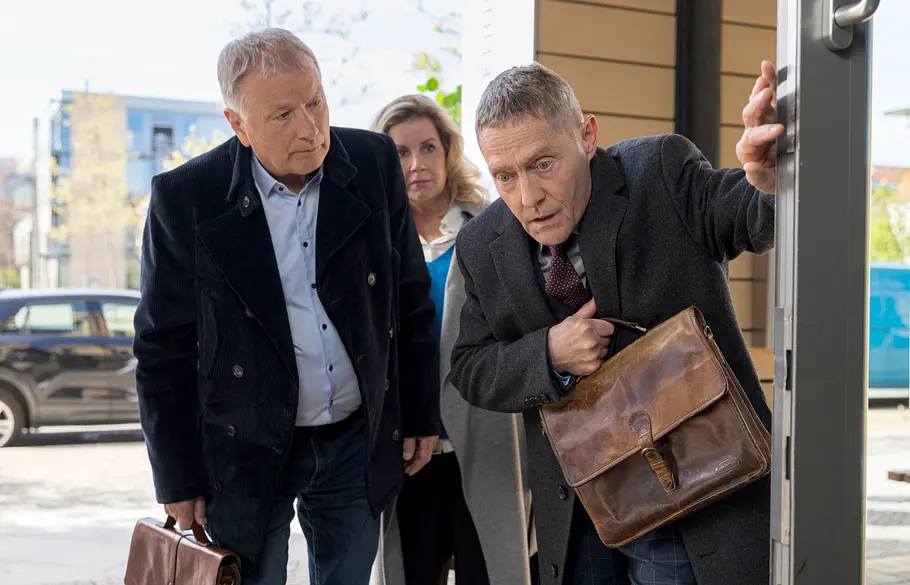 In aller Freundschaft Folge 1155 Dr. Rolf Kaminski stützt sich mit einer Ledertasche am Türrahmen ab. Dr. Roland Heilmann und Sarah Marquardt stehen daneben.