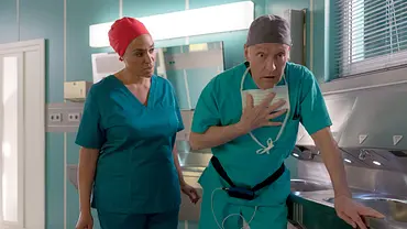 Dr. Lucia Böhm sieht zu Dr. Rolf Kaminski, der in OP-Kleidung eine Hand an die Brust hält und sich am Waschbecken abstützt. - Foto: © MDR/Rudolf Wernicke