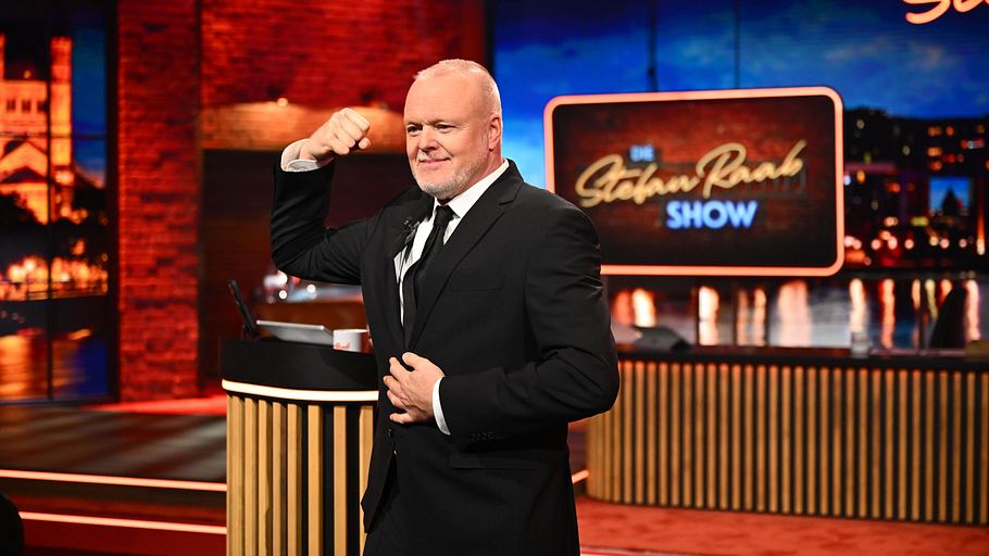 Stefan Raab trägt einen schwarzen Anzug und präsentiert seine Muskeln.