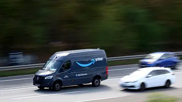Ein dunkelblauer Amazon-Prime-Lieferwagen fährt neben einem weißen und einem blauen Auto auf einer mehrspurigen Straße. - Foto: IMAGO / Jan Huebner Ein dunkelblauer Amazon-Prime-Lieferwagen fährt neben einem weißen und einem blauen Auto auf einer mehrspurigen Straße. - Foto: IMAGO / Jan Huebner