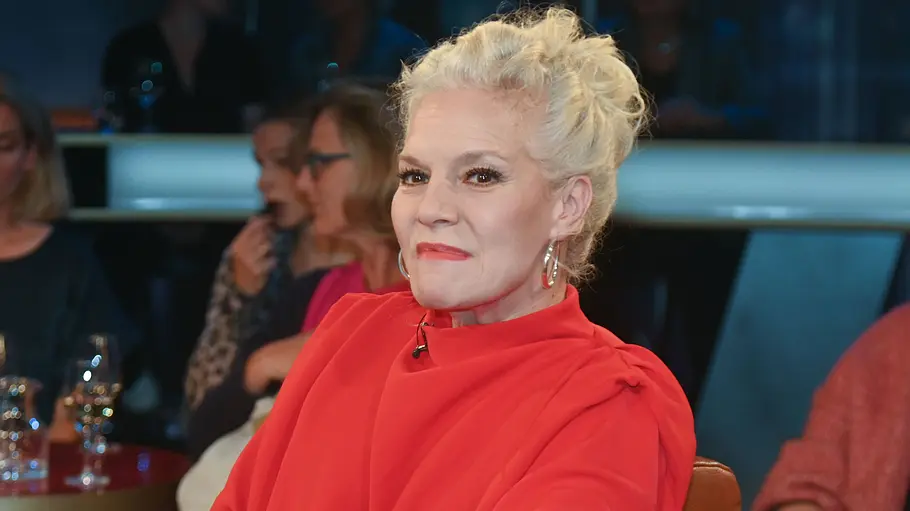 Ina Müller bei der NDR Talk Show Ina Müller sitzt in einem roten Oberteil in einer Gesprächsrunde und lächelt.