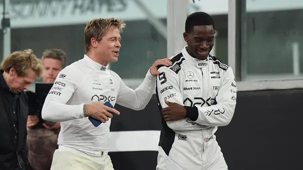 Brad Pitt und Damson Idris stehen in weißer Rennfahrermontur auf einer Rennstrecke.  - Foto: IMAGO / Eibner