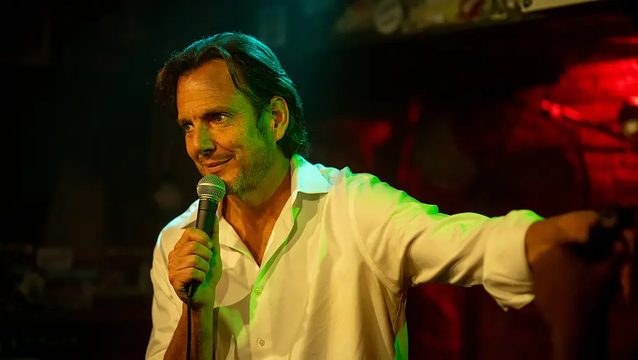 Alex (Will Arnett) steht auf einer Stand-Up-Comedy Bühne und spricht ins Mikro. Er lächelt leicht.