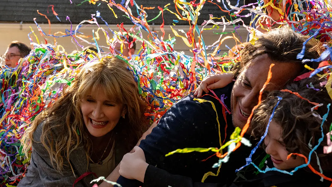 Laura Dern (Tess) und Will Arnett (Alex) mit ihrem Sohn werden von Papierkonfetti umhüllt.  - Foto: © 2025 Searchlight Pictures All Rights Reserved.