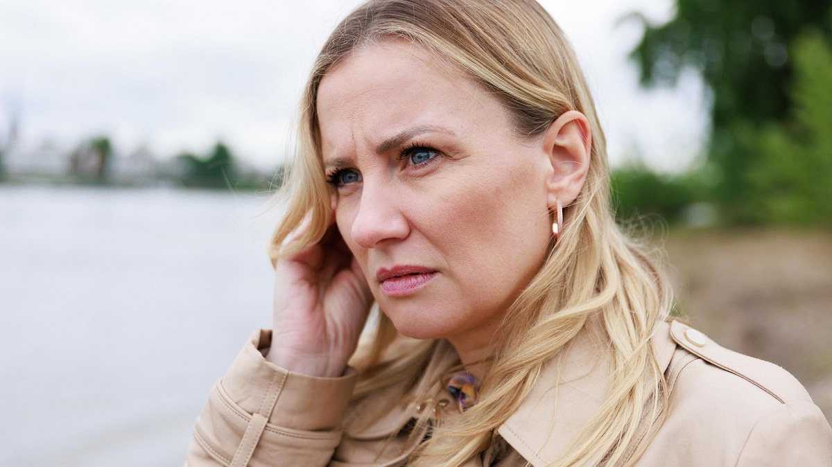 Erneut schlechte Nachrichten für Isabelle. Isabelle starrt mit ernstem Blick und Hand am Ohr in die Ferne.