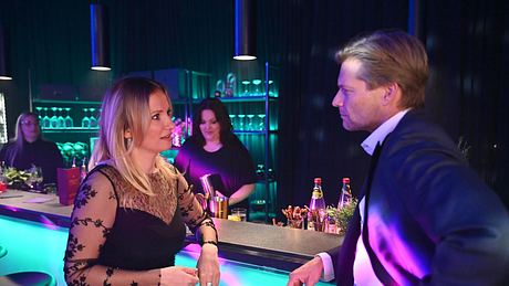 Isabelle im schwarzen Kleid mit ihrem neuen Schwarm Ilias im Anzug in der Bar. - Foto: RTL / Julia Feldhagen