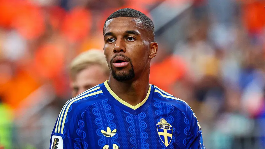 Fußballspieler der schwedischen Nationalmannschaft im blauen Trikot mit der Rückennummer 4 blickt während eines Länderspiels aufmerksam über den Platz. Im Hintergrund sind verschwommene Zuschauer in orangefarbenen Trikots zu sehen.