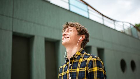 Mann grinst mit Apple EarPods und iPhone in der Hand. - Foto: istock / m-imagephotography