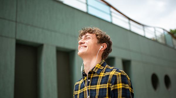 Mann grinst mit Apple EarPods und iPhone in der Hand. - Foto: istock / m-imagephotography