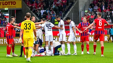 Auf dem Fußballfeld: Musiala liegt auf dem Boden und wird behandelt, die anderen Spieler stehen um ihn herum. - Foto: IMAGO / Nordphoto Auf dem Fußballfeld: Musiala liegt auf dem Boden und wird behandelt, die anderen Spieler stehen um ihn herum. - Foto: IMAGO / Nordphoto