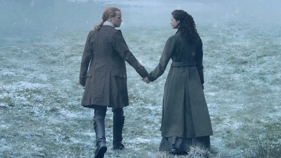 Jamie und Claire kehren dieses Jahr ein letztes Mal auf unsere Bildschirme zurück. Jamie und Claire gehen über eine verschneite Wiese.