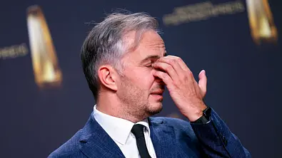 Jan Böhermann im blauen Anzug und mit dunkler Krawatte fasst sich bei geschlossenen Augen mit einer Hand an die Nasenwurzel. - Foto: IMAGO / Panama Pictures