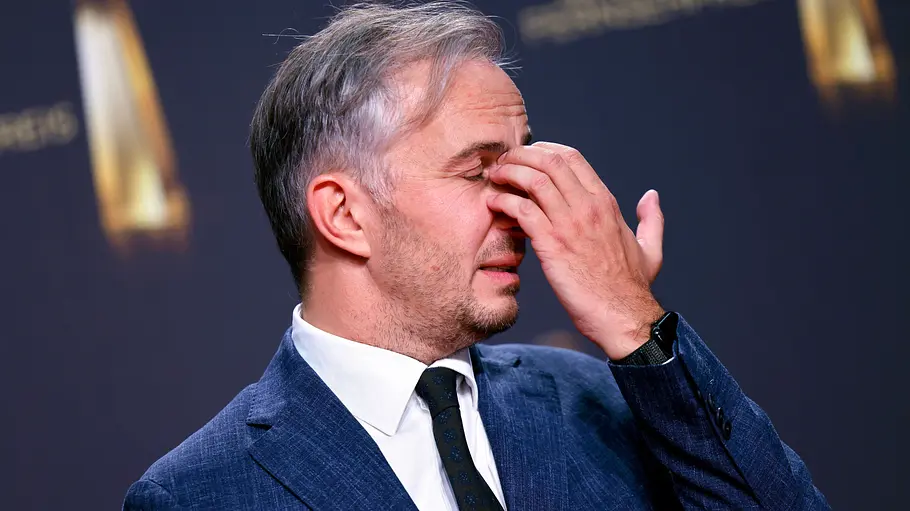 Jan Böhmermann spricht endlich Klartext zu TV-Aus: „Furchtbare Entscheidung“ Jan Böhermann im blauen Anzug und mit dunkler Krawatte fasst sich bei geschlossenen Augen mit einer Hand an die Nasenwurzel.