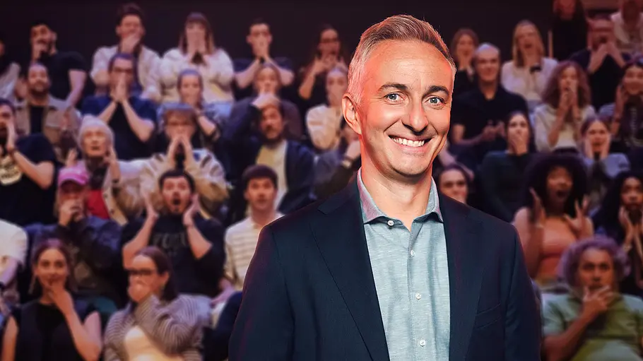Jan Böhmermann ZDF Lass dich überwachen Jan Böhmermann lächelt im dunklen Sakko vor einem Publikum, das teils die Hände vor Mund oder Gesicht hält.