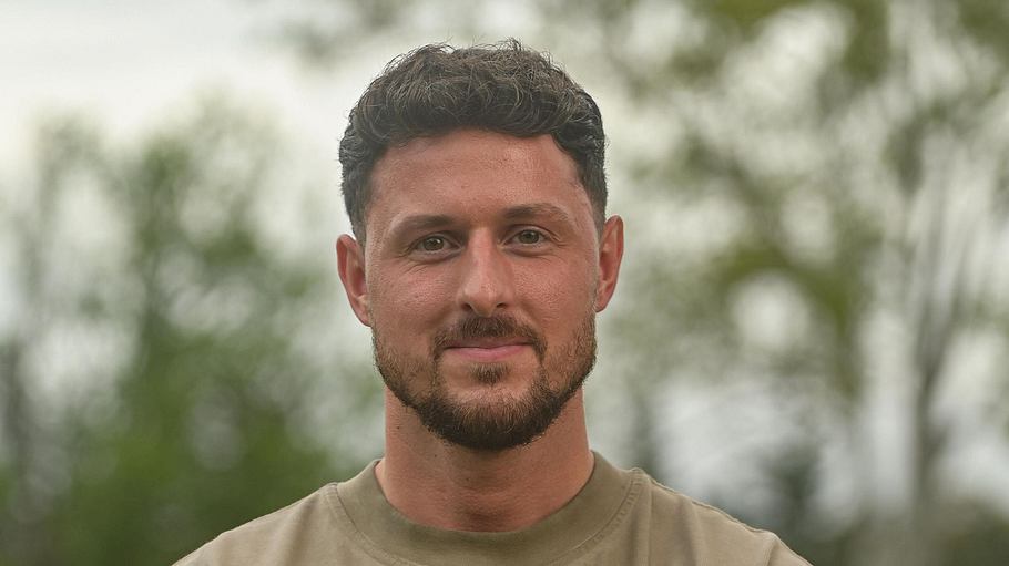 Jannik Kontalis in einem grünen T-Shirt, verschränkt die Arme und lächelt in die Kamera