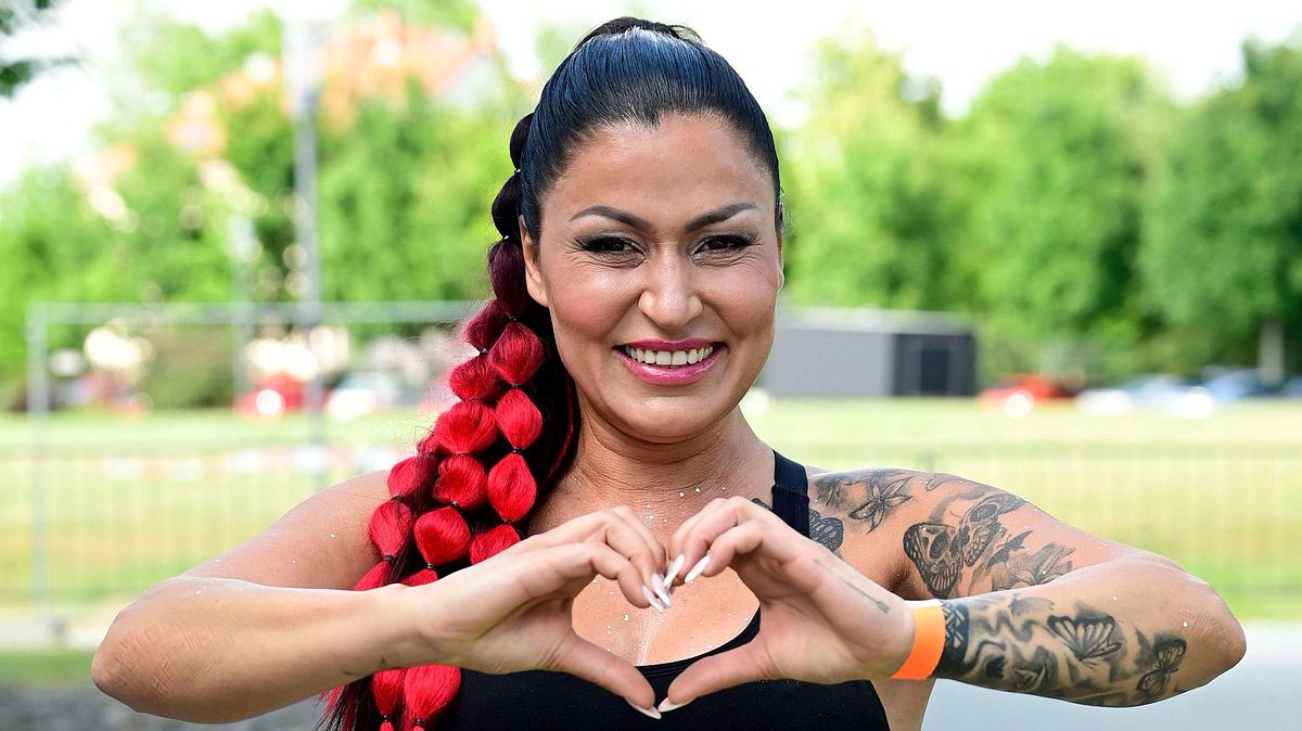 Jasmin Herren formt ein Herz mit ihren Fingern und lächelt breit in die Kamera.