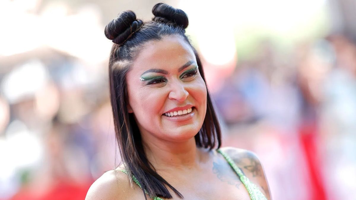 Jasmin Herren trägt zwei Space-Buns und grünen Lidschatten. Sie wird breit lächelnd von der Seite abgelichtet.
